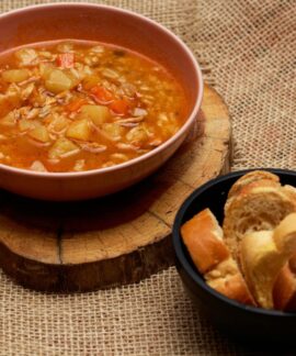 Warm vegetable soup and bread served on rustic surface, perfect for cozy meals.