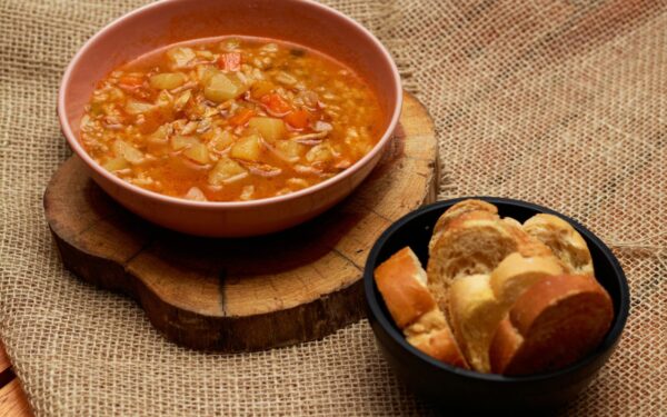 Warm vegetable soup and bread served on rustic surface, perfect for cozy meals.