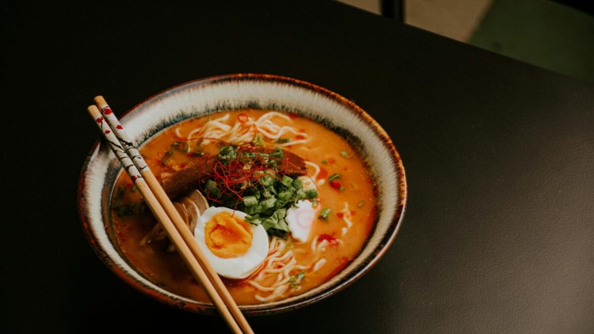 Close-up of gourmet ramen with egg and fresh greens in a bowl with chopsticks.
