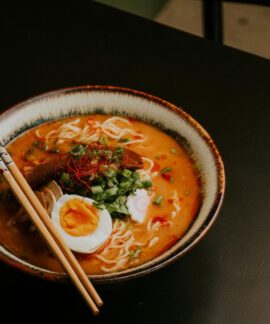 Close-up of gourmet ramen with egg and fresh greens in a bowl with chopsticks.