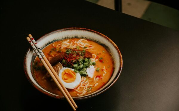 Close-up of gourmet ramen with egg and fresh greens in a bowl with chopsticks.