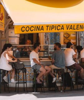 People enjoying food at a Valencian street stall under a bright yellow awning.