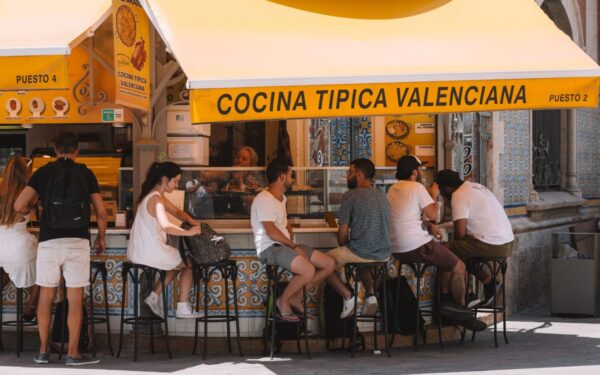 People enjoying food at a Valencian street stall under a bright yellow awning.