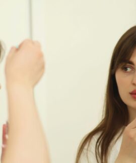 A young woman applying skincare serum in front of a mirror indoors. Perfect for beauty and self-care themes.