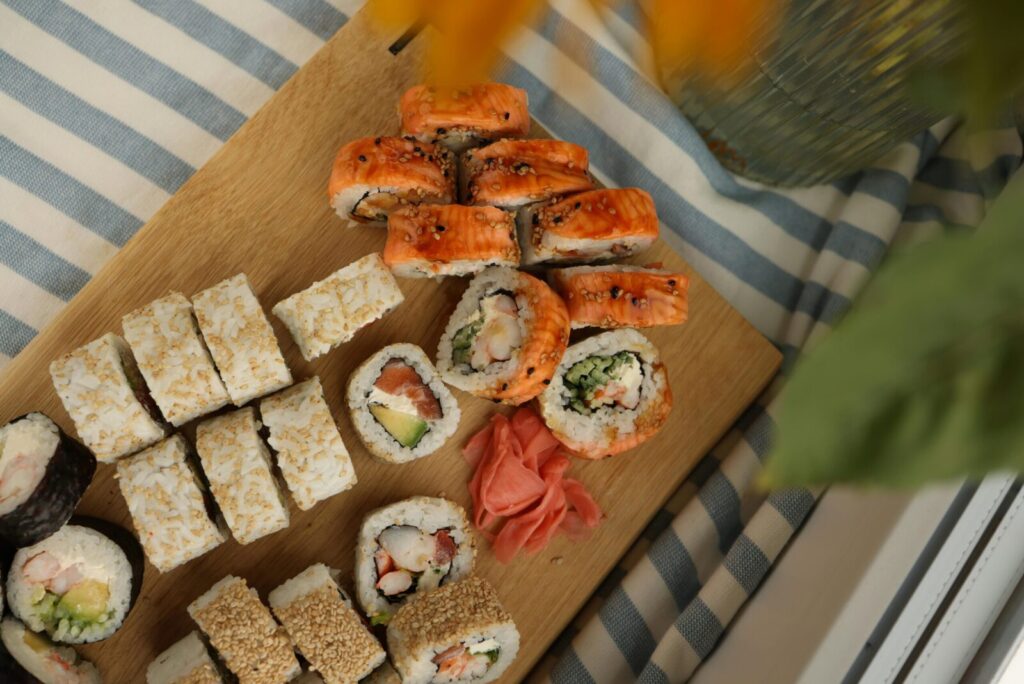 Top view of assorted sushi rolls with ginger on a wooden board.
