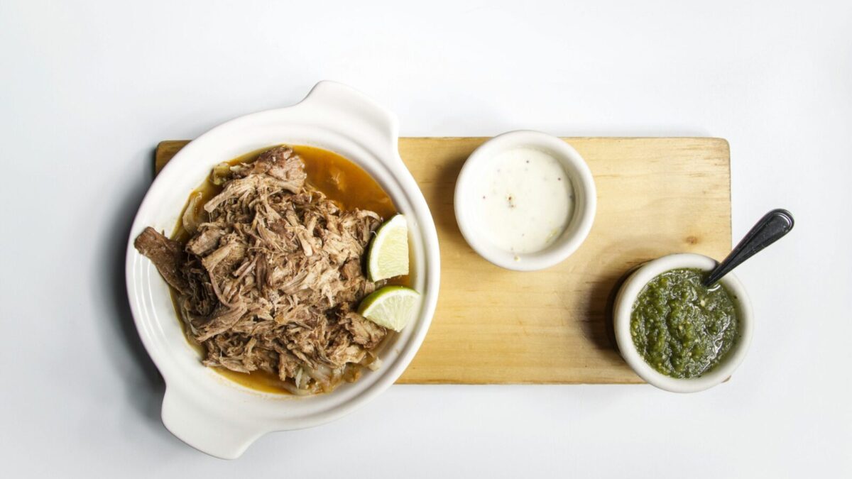 Top view of shredded meat with lime and sauces on a wooden platter, perfect for food presentations.