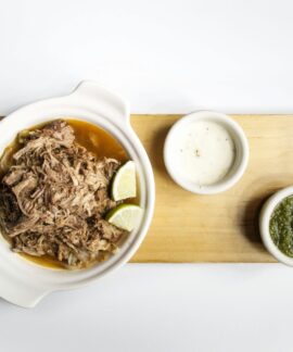 Top view of shredded meat with lime and sauces on a wooden platter, perfect for food presentations.