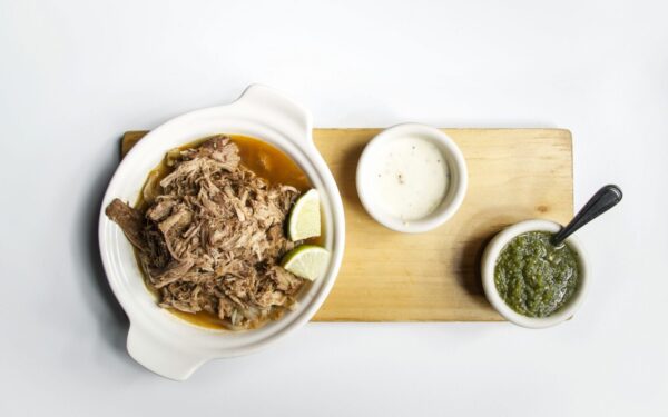 Top view of shredded meat with lime and sauces on a wooden platter, perfect for food presentations.