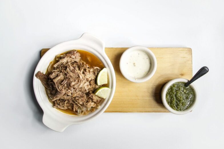 Top view of shredded meat with lime and sauces on a wooden platter, perfect for food presentations.