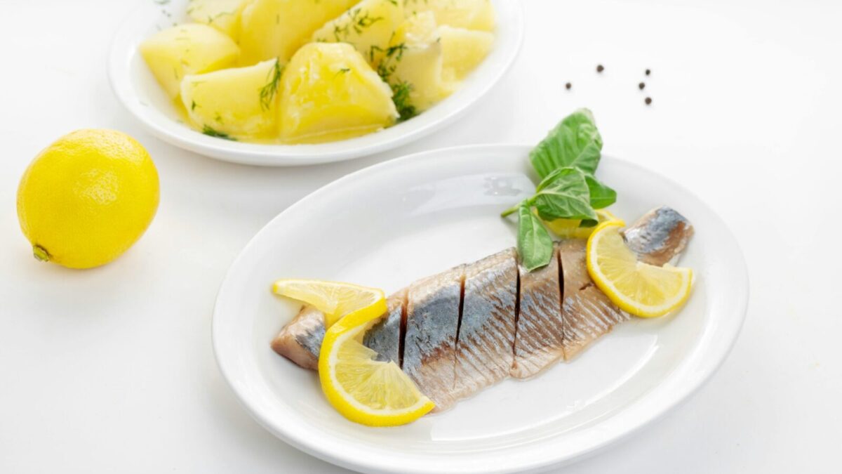 Delicious fish fillet with lemon slices and herb potatoes on white plates.