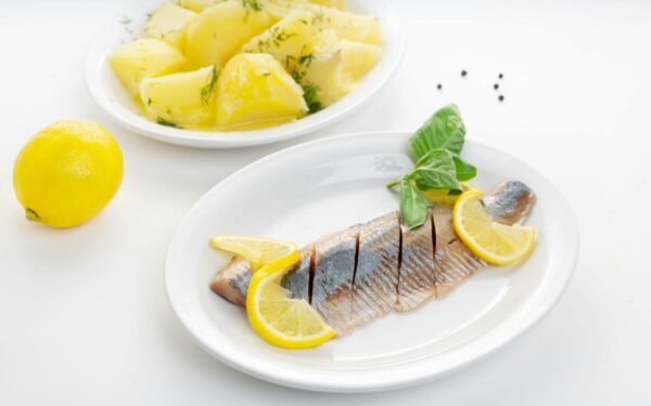 Delicious fish fillet with lemon slices and herb potatoes on white plates.