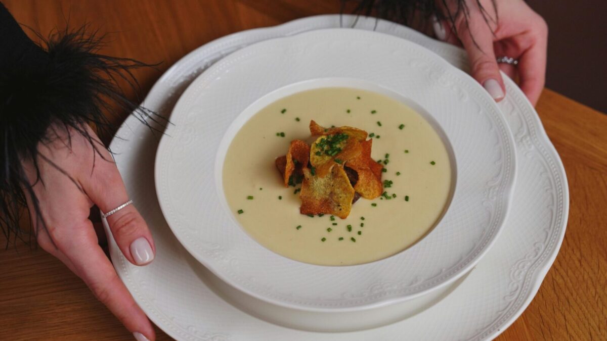 A gourmet creamy soup garnished with crispy toppings is beautifully served on white porcelain.