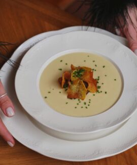 A gourmet creamy soup garnished with crispy toppings is beautifully served on white porcelain.