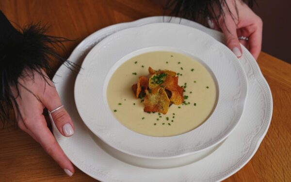 A gourmet creamy soup garnished with crispy toppings is beautifully served on white porcelain.