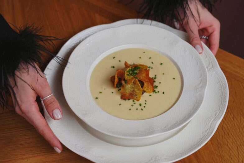 A gourmet creamy soup garnished with crispy toppings is beautifully served on white porcelain.