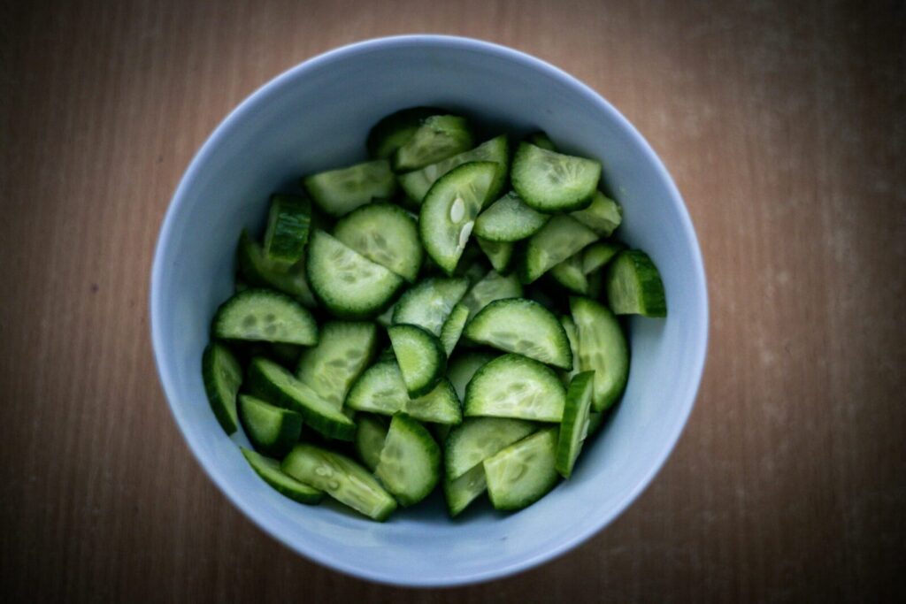 Top view of freshly chopped green cucumbers in a crisp white bowl on a wooden surface.