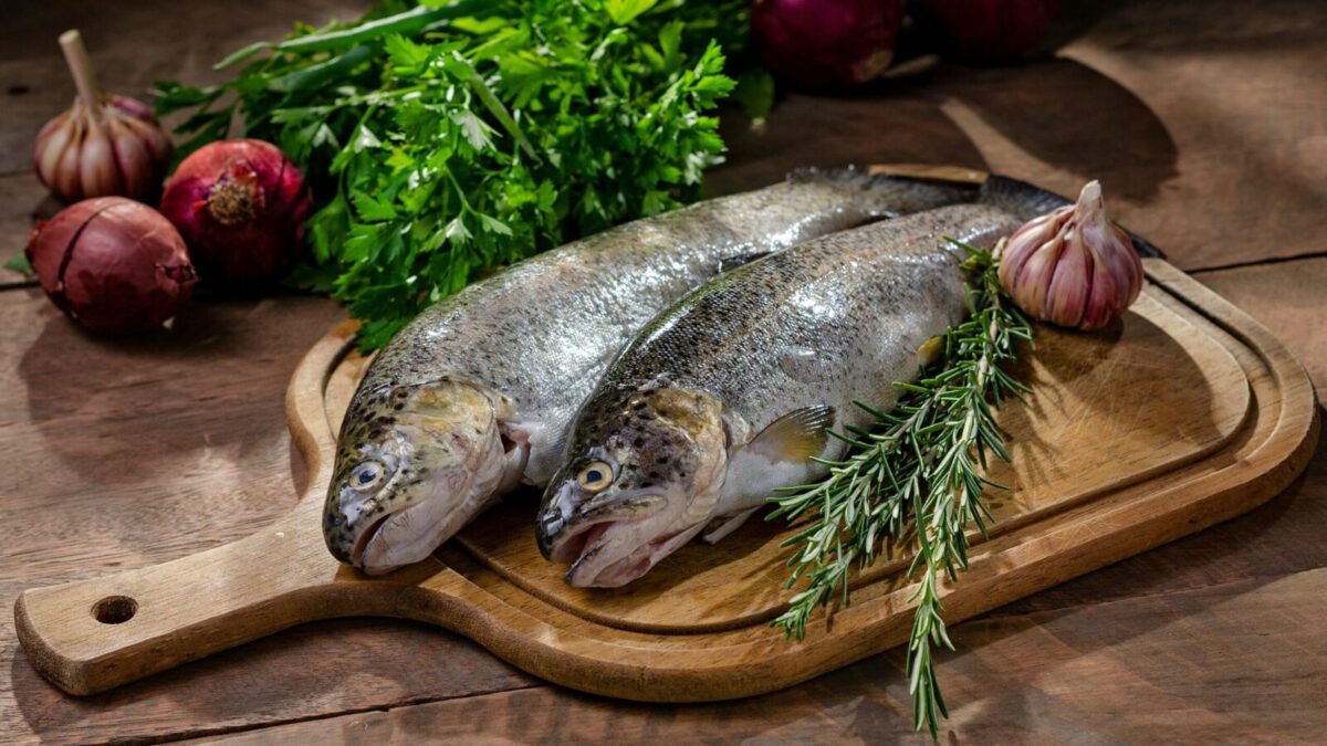 Two fresh raw fish with garlic, rosemary, and onions on wooden board.