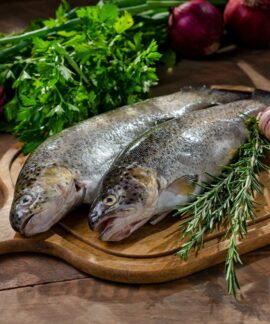 Two fresh raw fish with garlic, rosemary, and onions on wooden board.