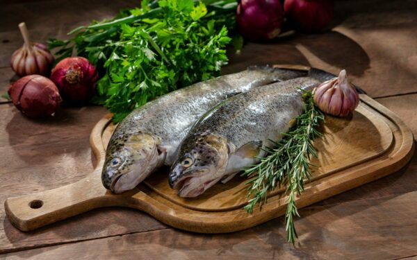 Two fresh raw fish with garlic, rosemary, and onions on wooden board.