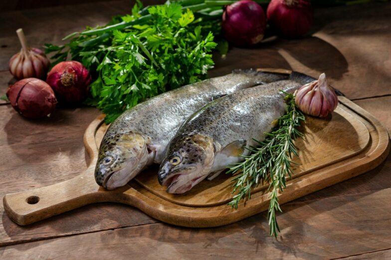 Two fresh raw fish with garlic, rosemary, and onions on wooden board.