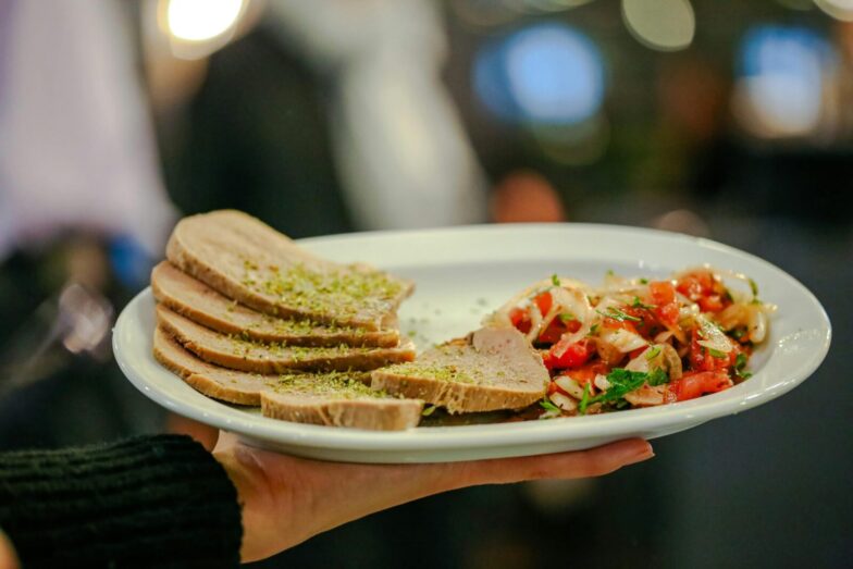 Close-up of a gourmet dish featuring beef tongue slices and fresh tomato salsa held by a server indoors.