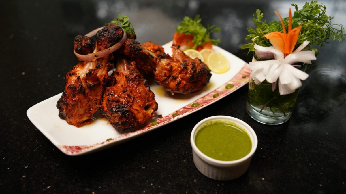 Delicious grilled chicken drumsticks served with green chutney and fresh vegetable garnish on a plate.