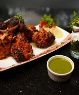 Delicious grilled chicken drumsticks served with green chutney and fresh vegetable garnish on a plate.