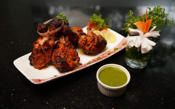 Delicious grilled chicken drumsticks served with green chutney and fresh vegetable garnish on a plate.