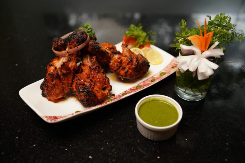 Delicious grilled chicken drumsticks served with green chutney and fresh vegetable garnish on a plate.