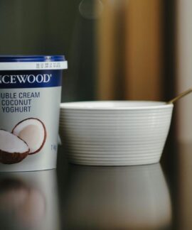 Lancewood double cream coconut yoghurt with a spoon and bowl on a reflective surface.