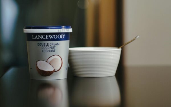 Lancewood double cream coconut yoghurt with a spoon and bowl on a reflective surface.