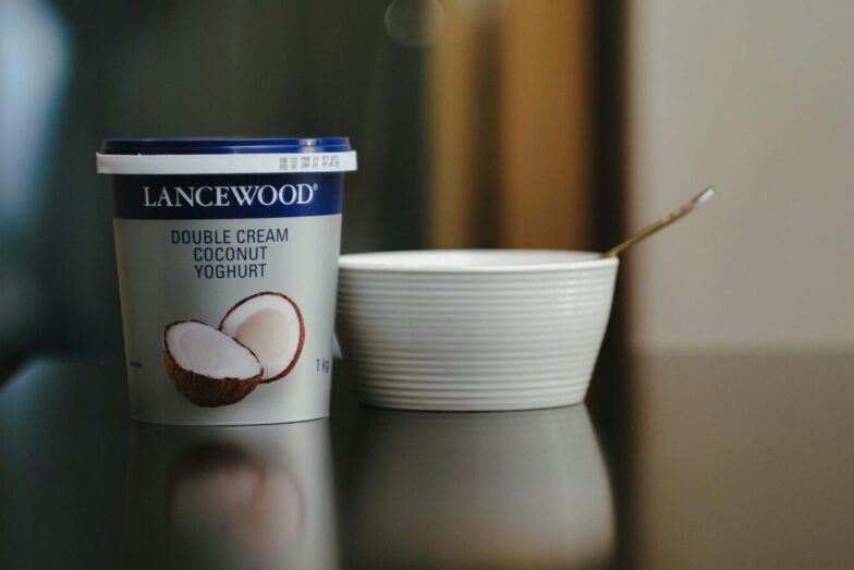 Lancewood double cream coconut yoghurt with a spoon and bowl on a reflective surface.