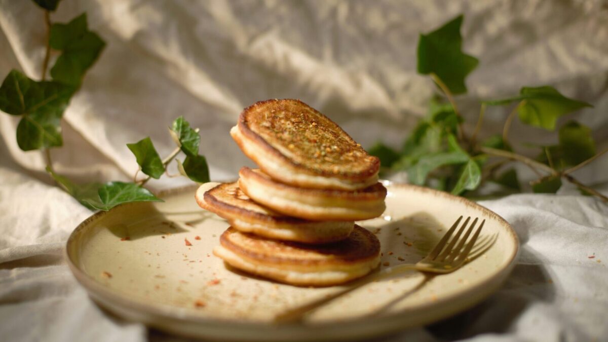 Close-up of a stack of pancakes on a plate with a fork, surrounded by green leaves.