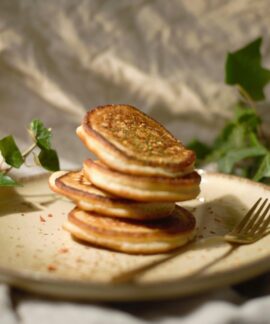 Close-up of a stack of pancakes on a plate with a fork, surrounded by green leaves.