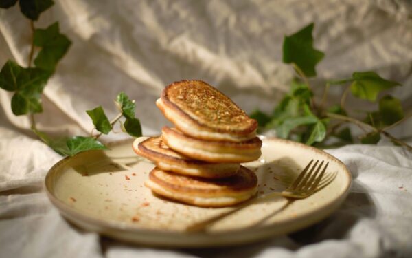 Close-up of a stack of pancakes on a plate with a fork, surrounded by green leaves.