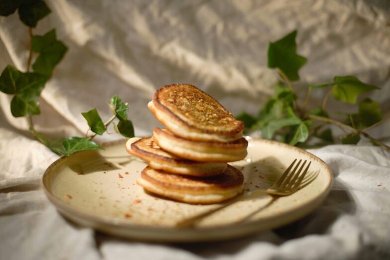 Close-up of a stack of pancakes on a plate with a fork, surrounded by green leaves.