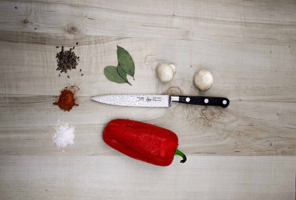 A high angle shot of fresh cooking ingredients including a bell pepper, mushrooms, and spices on a wooden board.