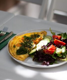 Delicious omelette accompanied by a fresh salad on a white plate, perfect for a healthy meal.