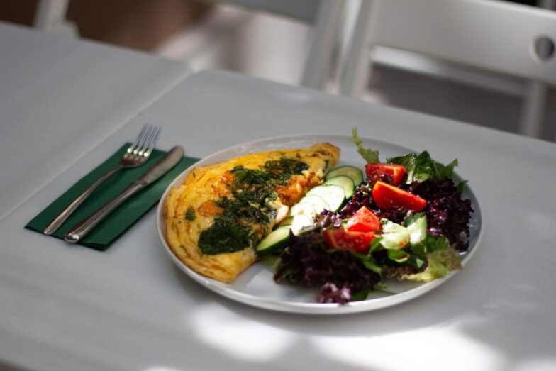 Delicious omelette accompanied by a fresh salad on a white plate, perfect for a healthy meal.
