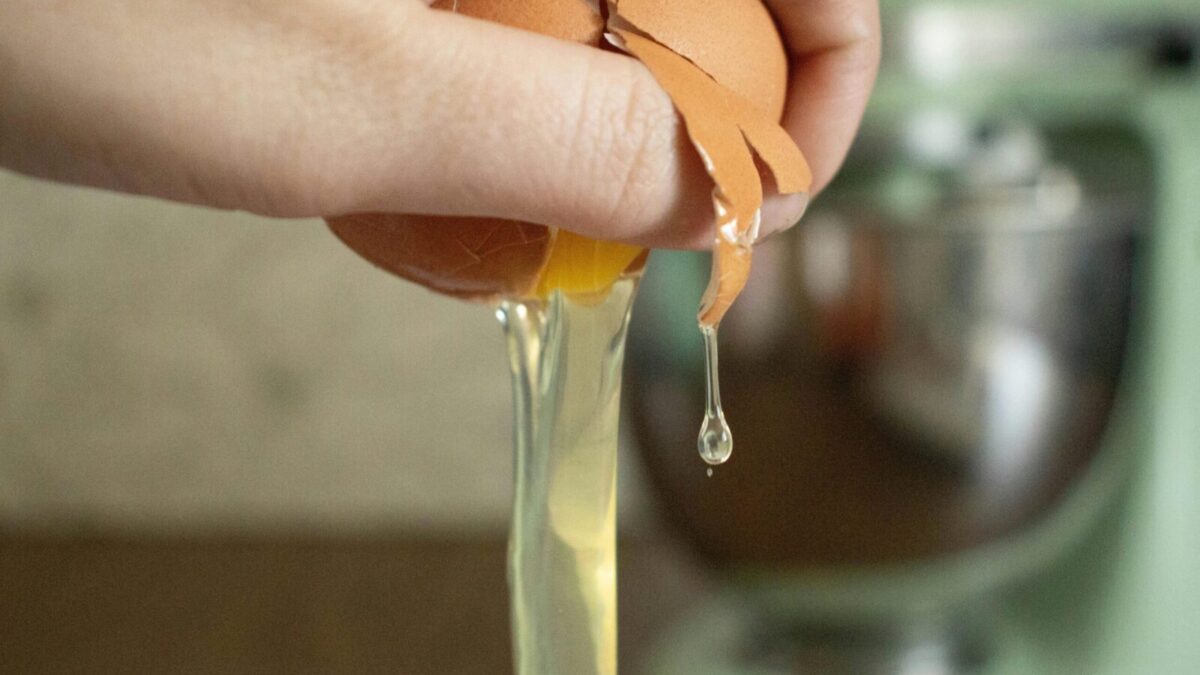 A hand cracks an egg over a bowl, preparing ingredients for baking.