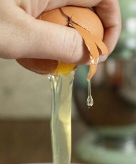A hand cracks an egg over a bowl, preparing ingredients for baking.