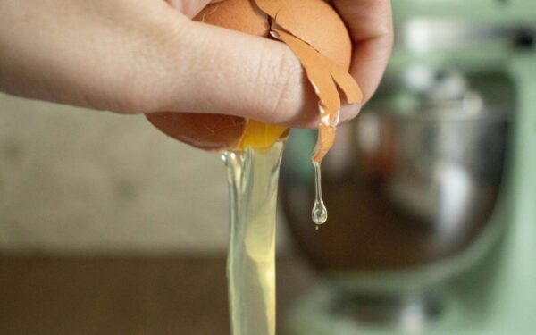 A hand cracks an egg over a bowl, preparing ingredients for baking.