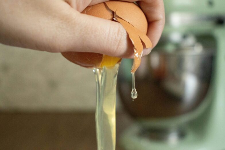 A hand cracks an egg over a bowl, preparing ingredients for baking.