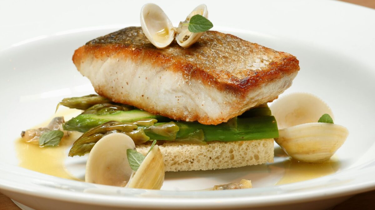 A gourmet fish dish served with clams and asparagus on a white plate.