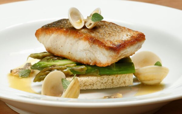 A gourmet fish dish served with clams and asparagus on a white plate.