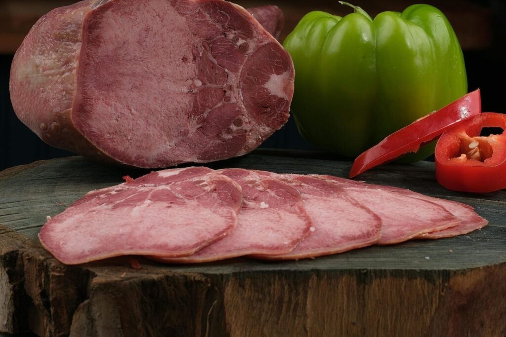 High-quality food photography showcasing sliced cured meat and fresh bell peppers on a rustic wooden board.