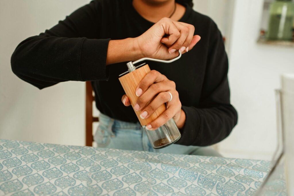 A person using a manual coffee grinder in a cozy indoor setting.