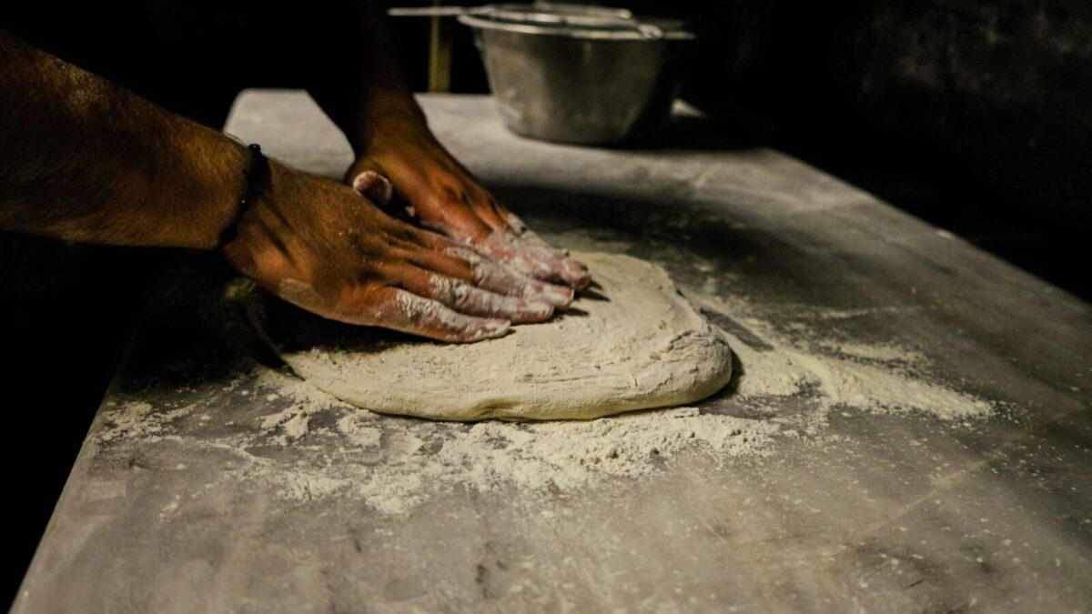 Close-up of a man kneading dough on a floured table in a traditional setting.