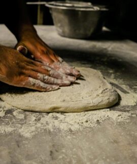 Close-up of a man kneading dough on a floured table in a traditional setting.