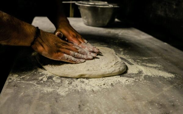 Close-up of a man kneading dough on a floured table in a traditional setting.